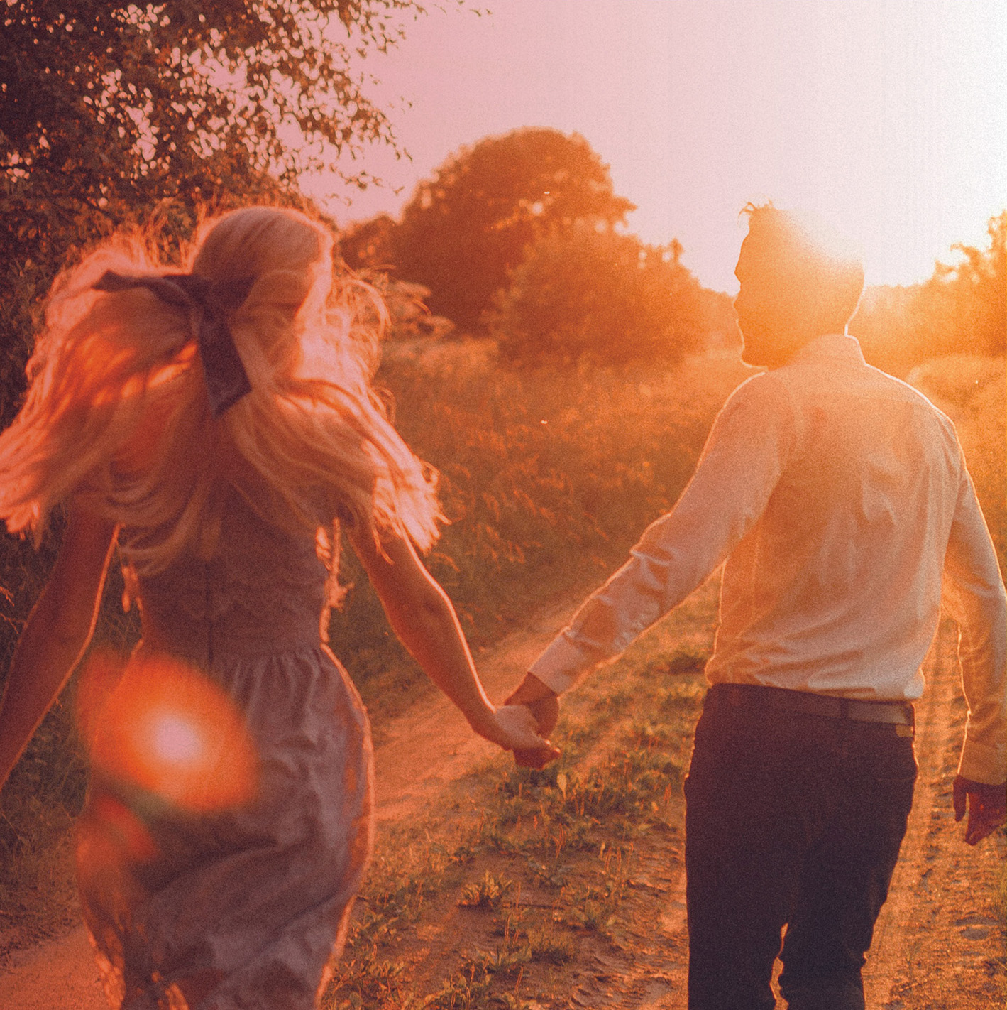 Couple walking hand-in-hand toward a golden sunset.